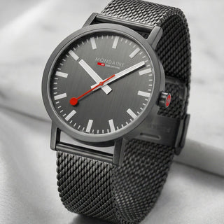 Gray wristwatch with a gray mesh band on a light gray background
